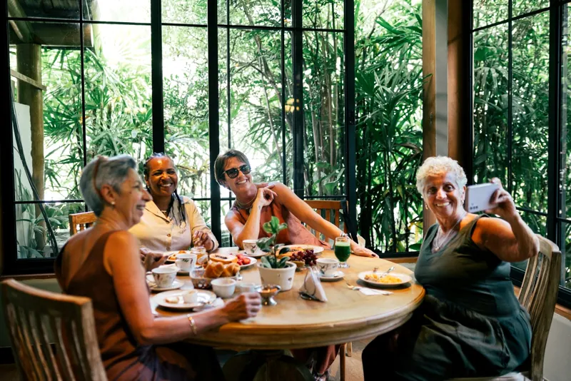 Hóspedes reunidas à mesa do café da manhã, com a mata ao fundo